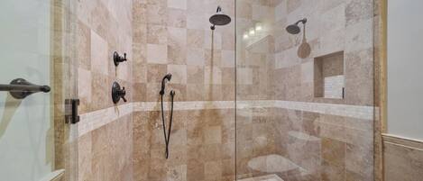 A glass-enclosed shower with multiple showerheads and a tiled floor.