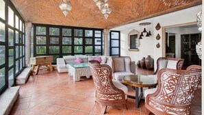 A spacious room with a tiled floor, a sofa, two patterned chairs, a small table, and a large window with a view of greenery. - Quinta Tere Country House (Zapopan)