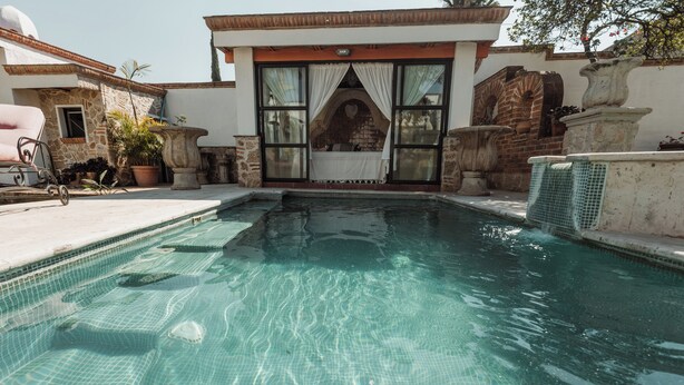 A swimming pool with a stone wall and a window with curtains. - Quinta Tere Country House (Zapopan)