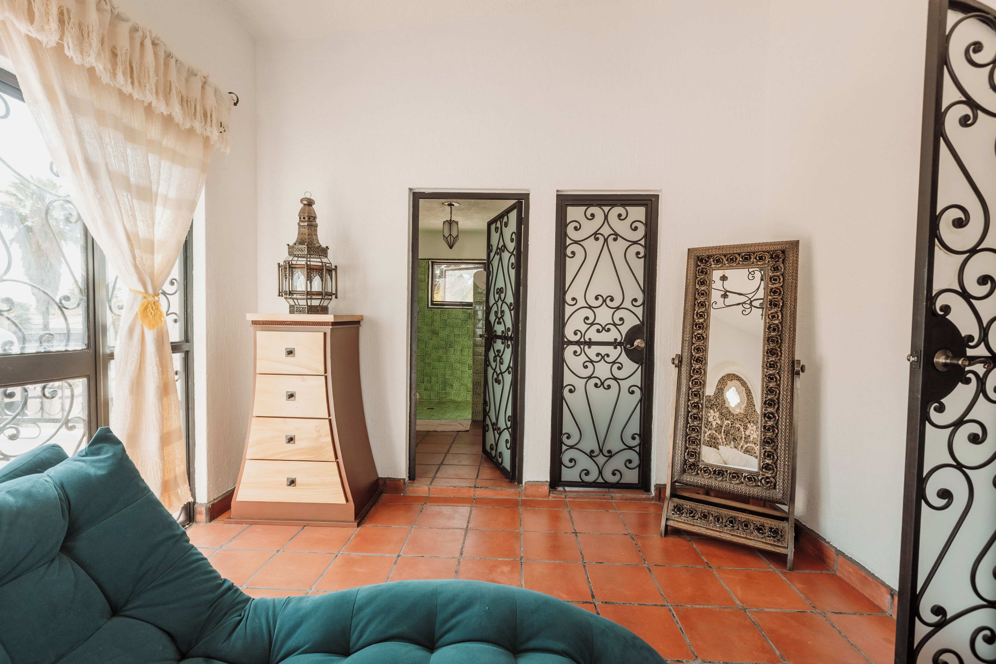 A room with a teal sofa, a wooden dresser, a lantern, and a mirror with ornate metalwork.