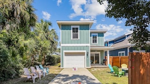 A two-story house with a garage, surrounded by a garden with various plants and outdoor furniture. - Pet Friendly East Hill New Build - Walk to Graffiti Bridge - Close to Downtown and Pensacola Beach (Pensacola)