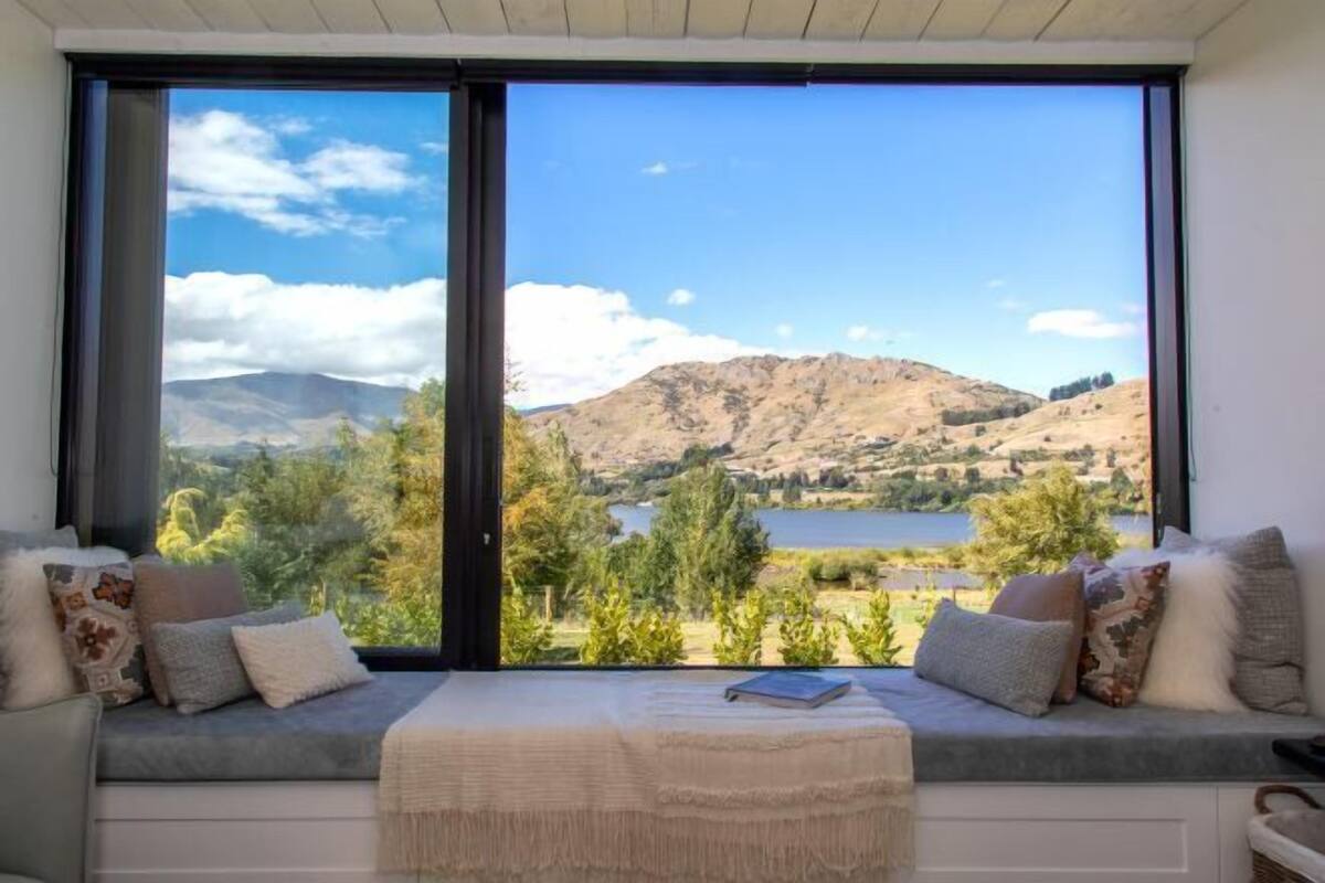 Een kamer met een groot raam met uitzicht op een meer en bergen.