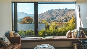 Una habitación con un amplio ventanal que ofrece vistas a la montaña, un banco acolchado y un sofá con cojines decorativos.