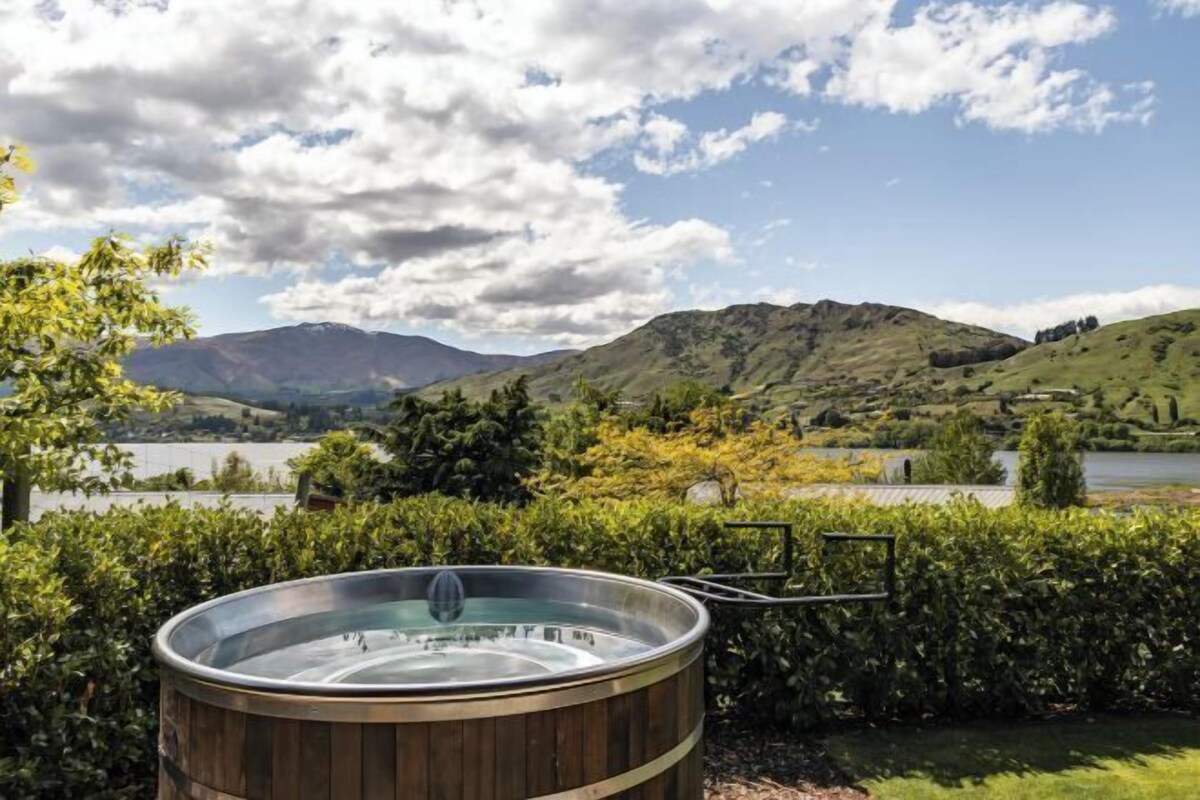Un jacuzzi en un jardín ajardinado con un lago y montañas al fondo.