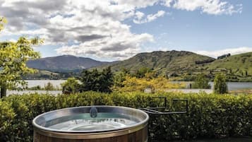 A hot tub in a landscaped garden with a lake and mountains in the background.