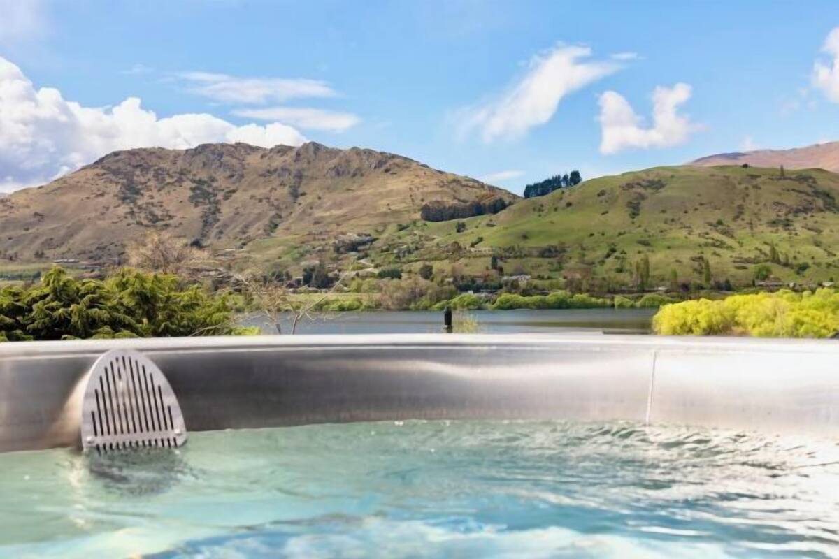 Een hottub met uitzicht op de bergen, omgeven door groen en een heldere lucht.