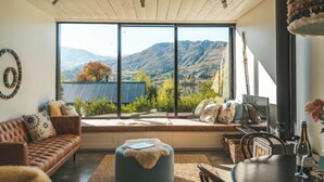 Una habitación acogedora con un ventanal grande que da a un paisaje montañoso, un sofá cómodo, una mesa de comedor con una botella de vino y un techo rústico.