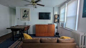 Una sala de estar con una mesa de comedor, un sofá, un televisor y un ventilador de techo.