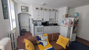 Un espacio habitable compacto con kitchenette, un sofá marrón con cojines amarillos y un globo sobre un refrigerador blanco.