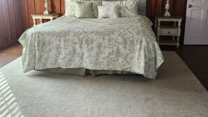 A bedroom with a wooden paneled wall, a bed with floral bedding, two bedside tables with lamps, and a carpeted floor. -  Farmhouse close to wedding venues, hunting plantations in Whigham - 3 bedrooms (Whigham)