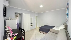 Quarto de hotel compacto com cama, sofá, escrivaninha e televisão.