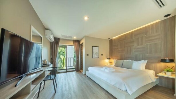A modern hotel room with a large bed, a flat-screen TV, a desk, and a balcony with a view of greenery.