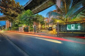 A street scene with a gated entrance, a palm tree, and a building with a sign. - Ralph Poshtel Pratunam (Bangkok)