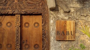 Una porta de fusta amb detalls escultòrics complexos i un rètol que diu Babu Villas.