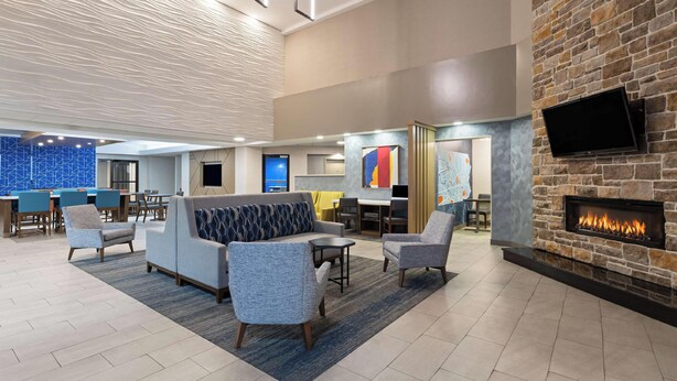 Eine Lobby mit einer Couch, Sesseln, einem Kamin, einem Fernseher und einer Wand mit blauem Muster.