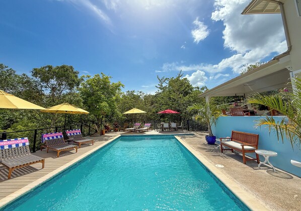 A swimming pool with lounge chairs and umbrellas, surrounded by greenery and a clear sky. - Beautiful Seascape Villa, Silver Sands Resort. Relax, recharge, and unwind! (Duncans)
