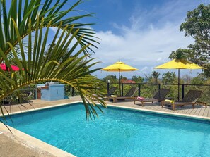 Una piscina con sillas de descanso y sombrillas amarillas, rodeada de vegetación y un cielo despejado.