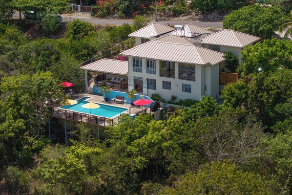 Una casa de varios pisos con piscina, rodeada de abundante vegetación.