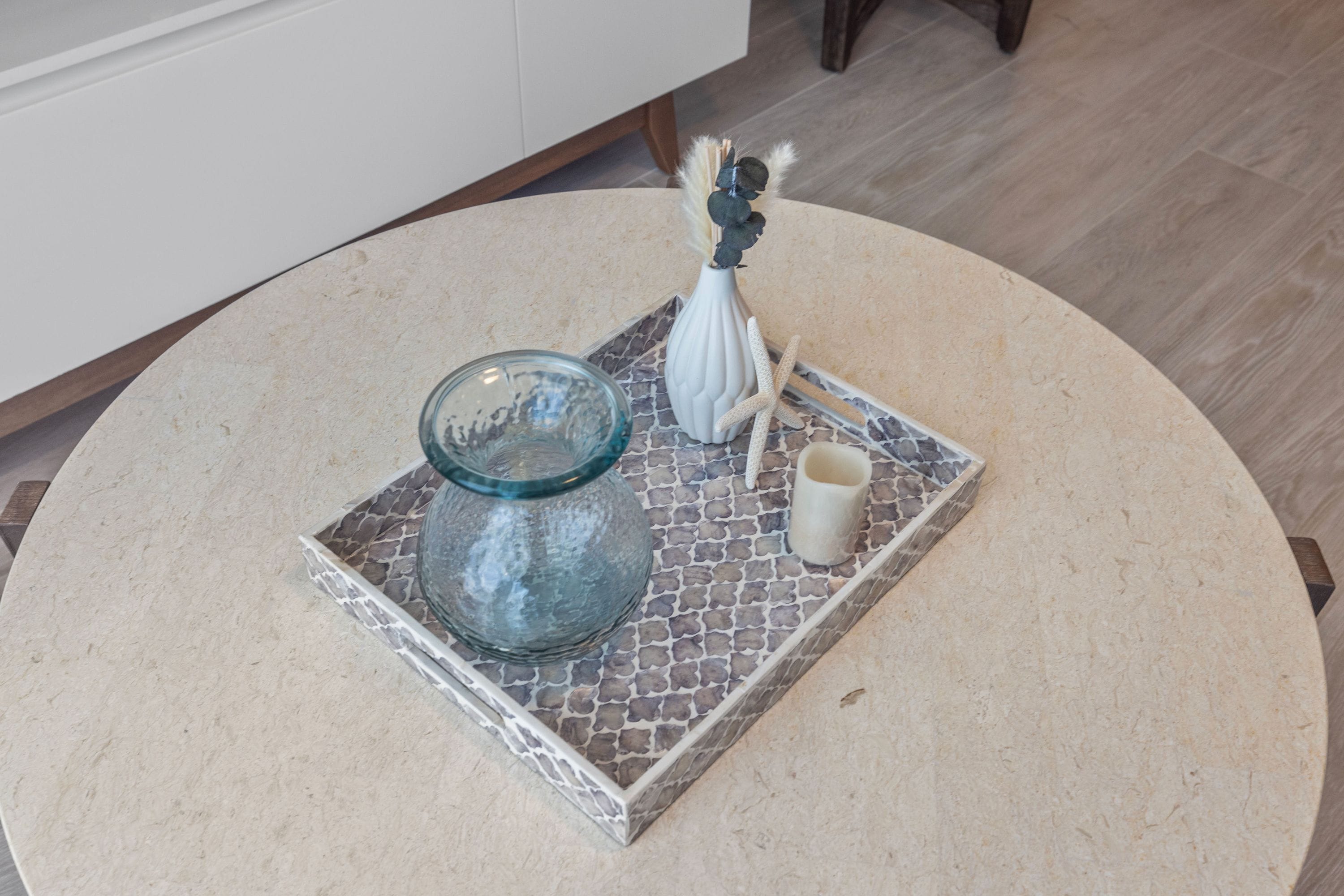 Un tavolo rotondo con un vaso di vetro, una candela bianca e una piccola ciotola su un vassoio decorato.