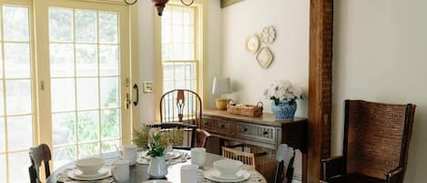 Zona pranzo con un tavolo rotondo apparecchiato per quattro persone, circondato da sedie in legno. Sopra il tavolo, un lampadario e, sulla parete, un mobile in legno con oggetti decorativi.