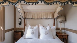 Quarto com cama de dossel, duas mesas de cabeceira, abajur e telefone fixado na parede.
