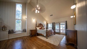 Une chambre spacieuse avec un grand lit, un plancher en bois, un coin lecture près de la fenêtre et une vue sur l’extérieur.