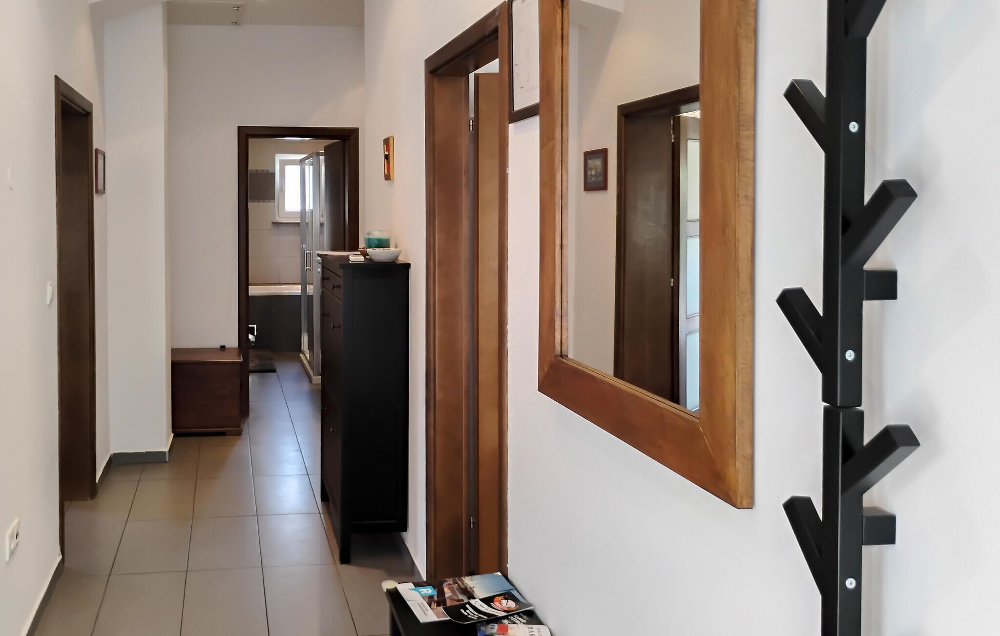 Un corridoio con stipite in legno, un attaccapanni nero e pavimento piastrellato.