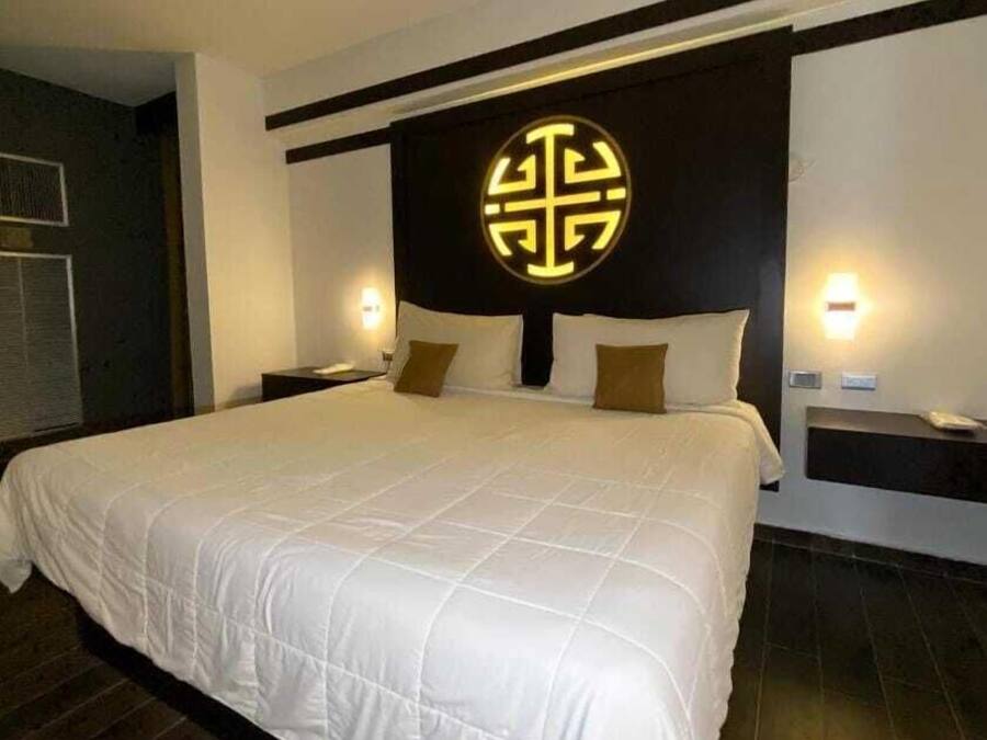 A large bed with a quilted white duvet, two bedside tables with lamps, and a decorative wall panel with a circular design.