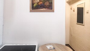 Keittiössä on liesi, pyöreä puupöytä ja seinällä oleva maalaus, jossa on kuvattuna hedelmiä.