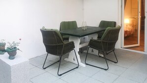 Pieni patio, jossa on pöytä ja neljä tuolia, ruukussa oleva kasvi sekä liukuovi, joka johtaa sisätilaan.