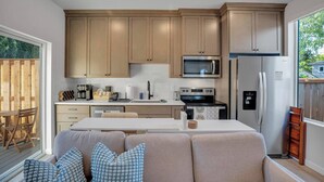 A modern kitchen with wooden cabinets, a microwave, a refrigerator, and a dining area with a sofa and cushions.