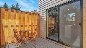 A wooden deck with a table and chairs, a sliding glass door, and a wooden fence.