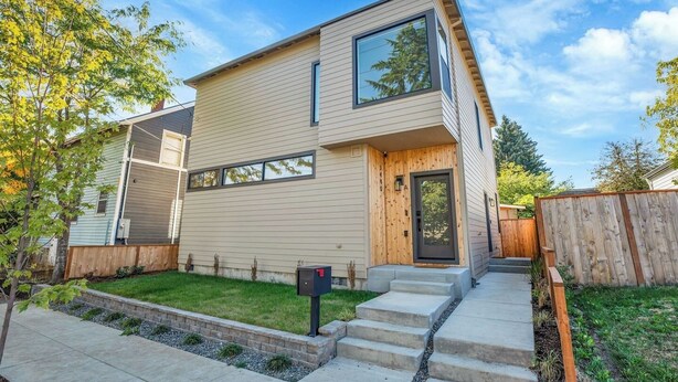 A modern two-story house with a large window, a front door, and a small front yard.