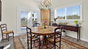Comedor con una mesa de madera, sillas, una araña y vistas a través de una ventana.