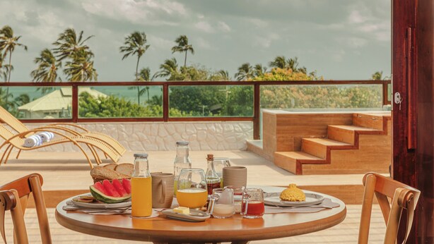 A breakfast table with various food items and drinks, overlooking a scenic view of palm trees and a cloudy sky. - Amana Icaraizinho (Amontada)