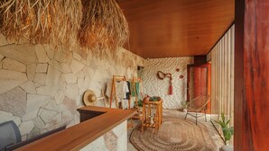 A room with a stone wall, wooden ceiling, and a woven rug. - Amana Icaraizinho (Amontada)