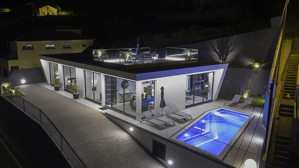 Una casa moderna con piscina en la azotea, puertas de vidrio y zona de estar exterior.