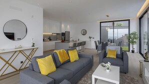 A modern living room with a grey sofa and yellow cushions, a white coffee table, and a large window offering a view of the outdoors. - A&M House III - Luxury Holidays Home (Arco da Calheta)