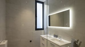 Un baño moderno con inodoro, tocador doble y un espejo grande.