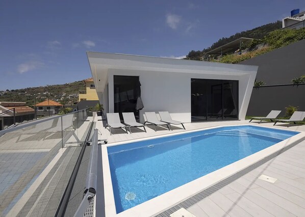 A rooftop swimming pool with lounge chairs and a modern building with glass doors.