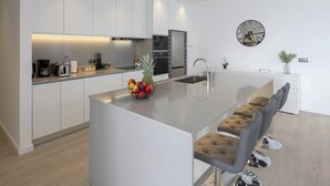 Una cocina moderna con armarios blancos, una isla central con frutero, electrodomésticos de acero inoxidable y un reloj redondo en la pared.
