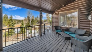 A wooden deck with a sofa and chairs, overlooking a forested area. - The Lost Creek Lodge - A Perfect Escape for Families, Reunions, and Friends. (Duck Creek Village)