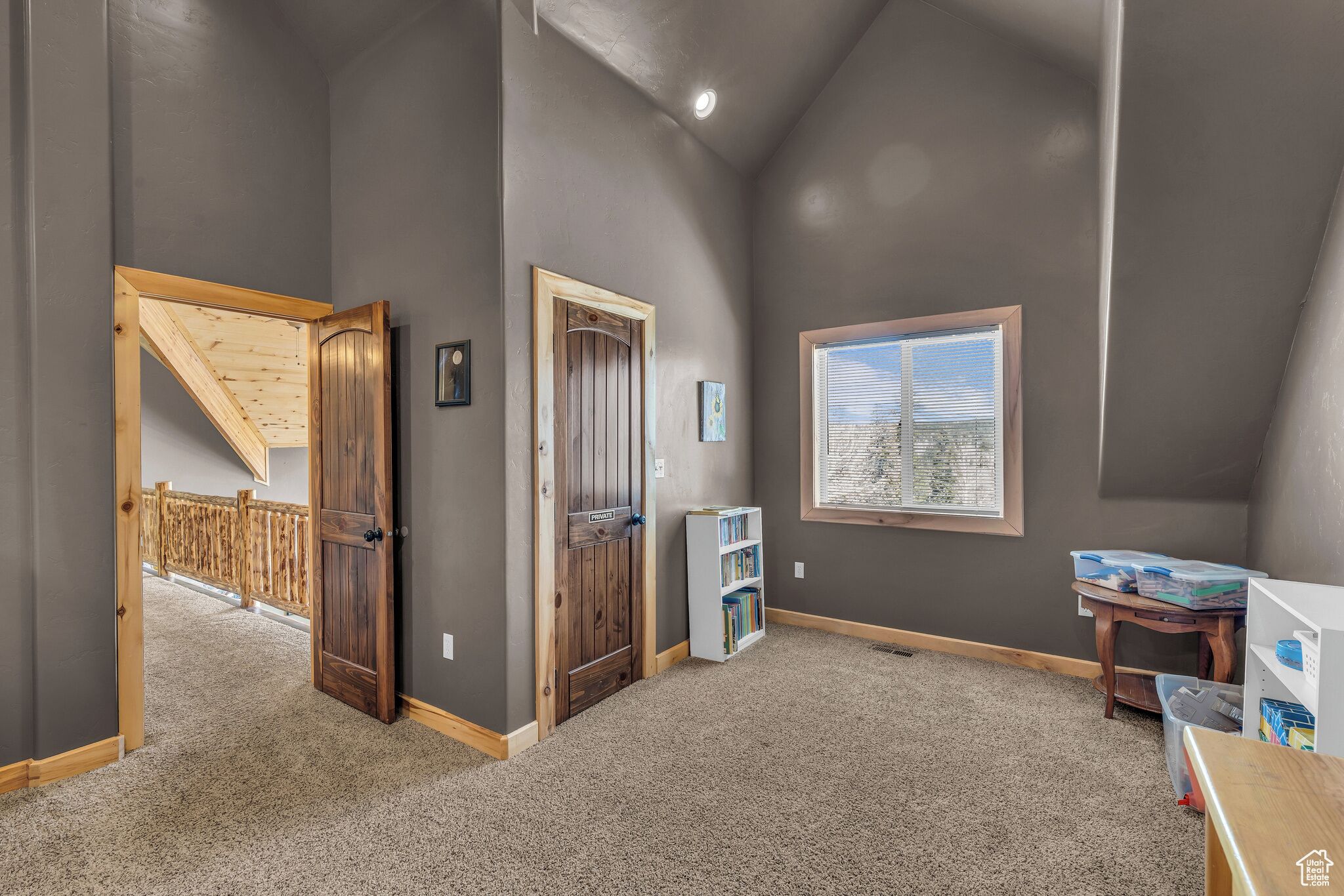 A room with a sloped ceiling, a wooden door, a window with blinds, and a bookshelf.
