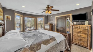 A bedroom with a large bed, a ceiling fan, a TV, and a wooden dresser. - The Lost Creek Lodge - A Perfect Escape for Families, Reunions, and Friends. (Duck Creek Village)