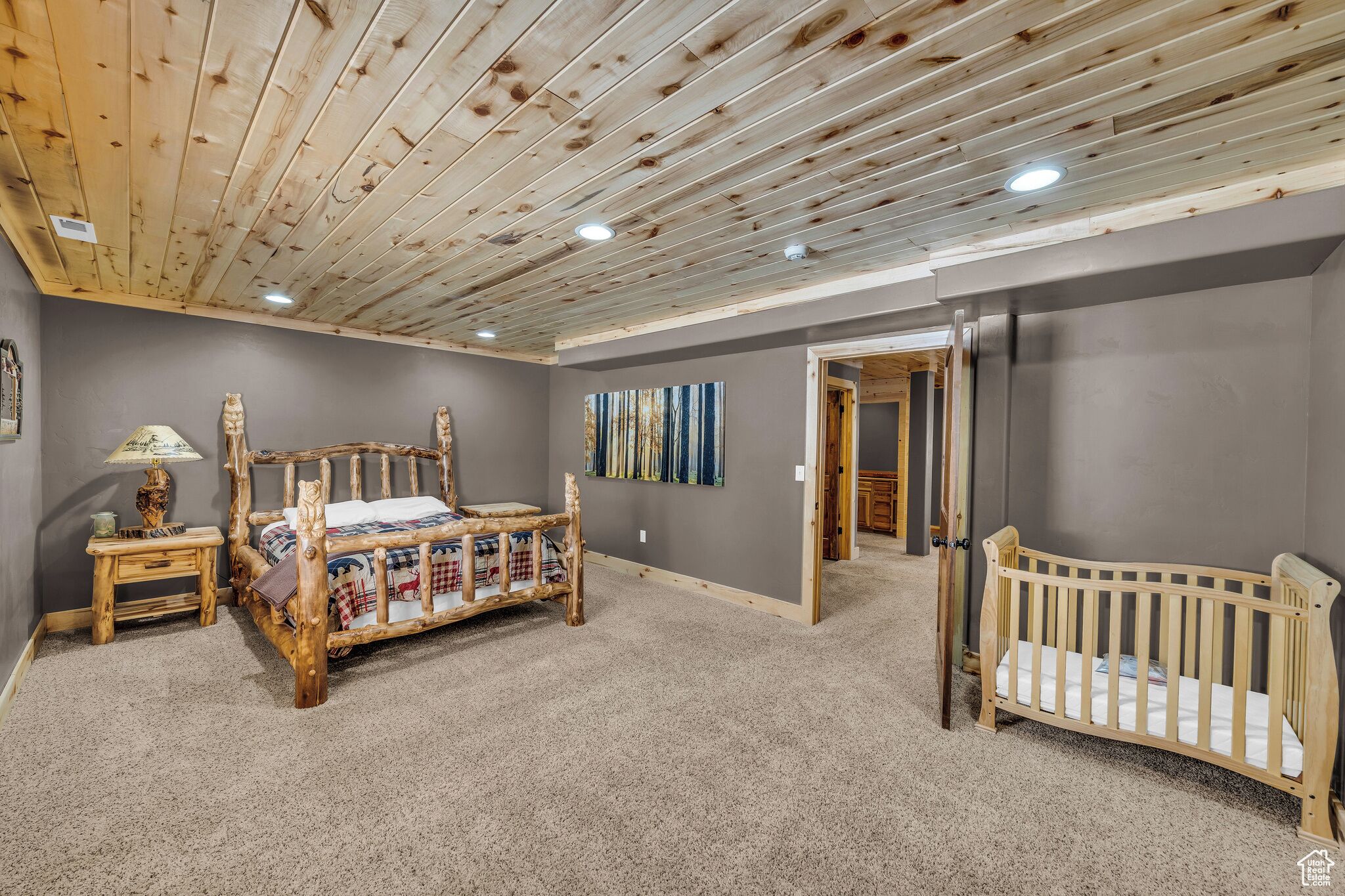 Una habitación con techo de madera, una cama, una cuna, un cuadro y una puerta que conduce a otra habitación.