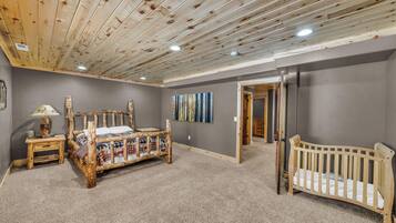 Una habitación con techo de madera, una cama, una cuna, un cuadro y una puerta que conduce a otra habitación.