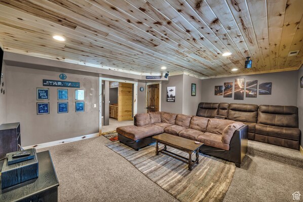 Un salón amplio con un sofá modular grande, una mesita de centro y un televisor. La habitación destaca por su techo de madera, una pared tem ática de Star Wars y cuadros enmarcados.