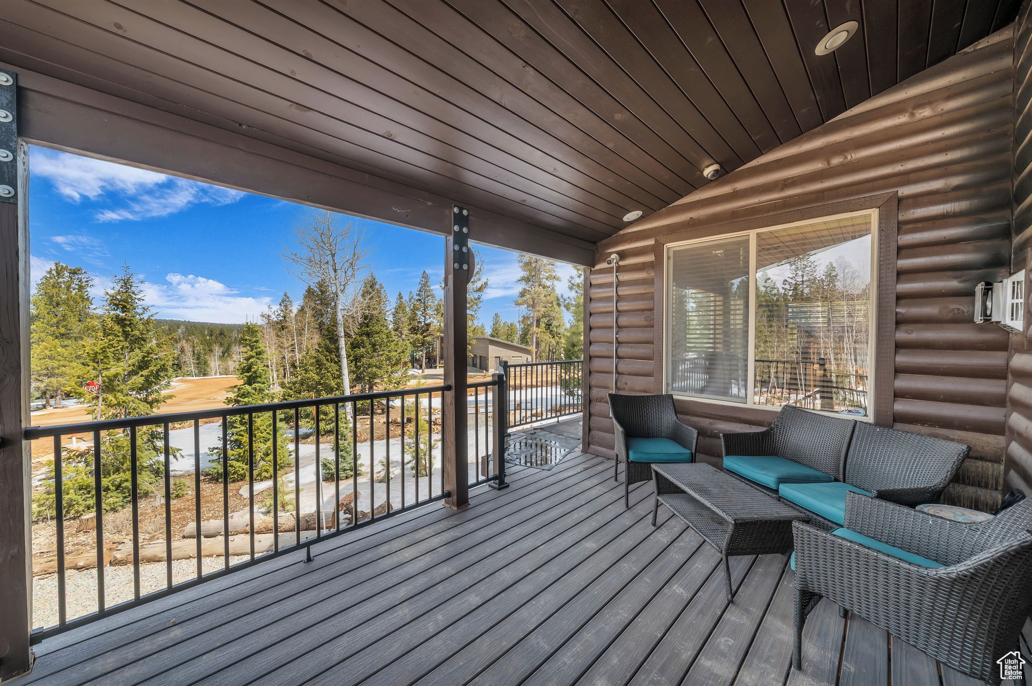 A wooden deck with a sofa and chairs, overlooking a forested area.
