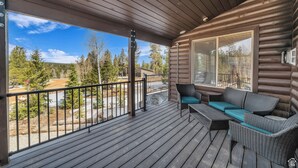 Une terrasse en bois avec un canapé et des fauteuils, donnant sur une zone boisée.