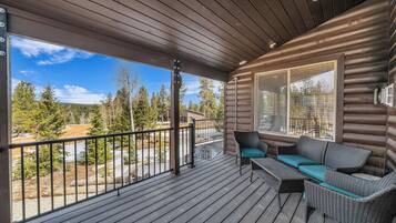 A wooden deck with a sofa and chairs, overlooking a forested area.